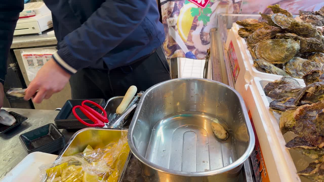 Un venditore apre ostriche fresche in una bancarella del mercato di Tokyo, utilizzando tecniche tradizionali di preparazione del pesce.