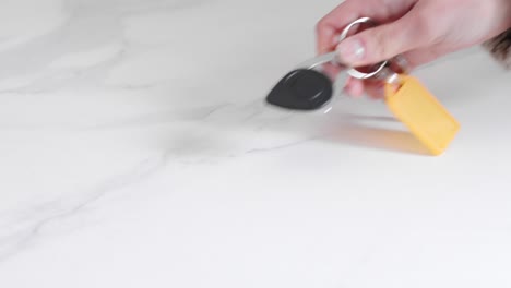 Young-Woman-Puts-Down-Keys-With-A-Keychain-On-Marble-Table