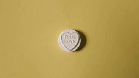 hand picking up heart candy with true love message on yellow background