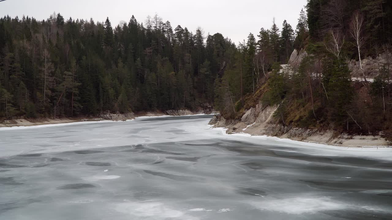 A serene winter scene showing the frozen surface of Lake Erlaufstausee in Styria, Austria. Surrounded by snow-covered trees and rugged cliffs, the ice reflects the calm, quiet environment.