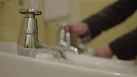 Washing-hands-in-a-public-washroom-sink-with-soap-dispenser