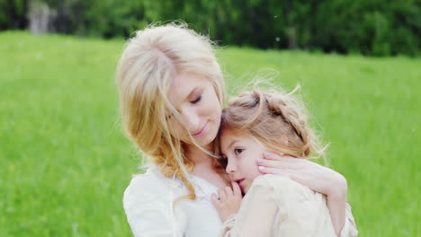 young blonde mother hugging her little daughter on a green lawn