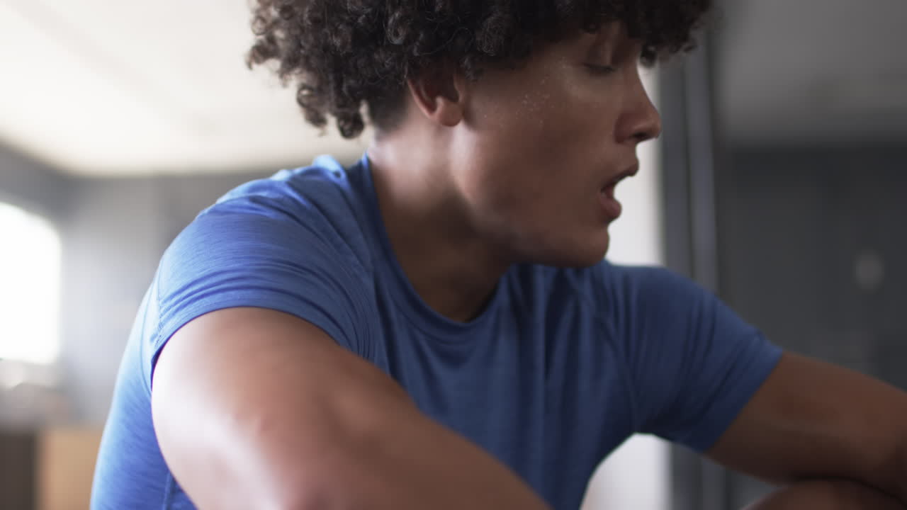 Exercising in gym, man in blue shirt looking to side, sweating