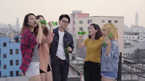 group of young asian women and man people dancing and raising their arms up in air to the music played by dj at sunset urban party on rooftop. young asian girls and boy friends hanging out with drinks