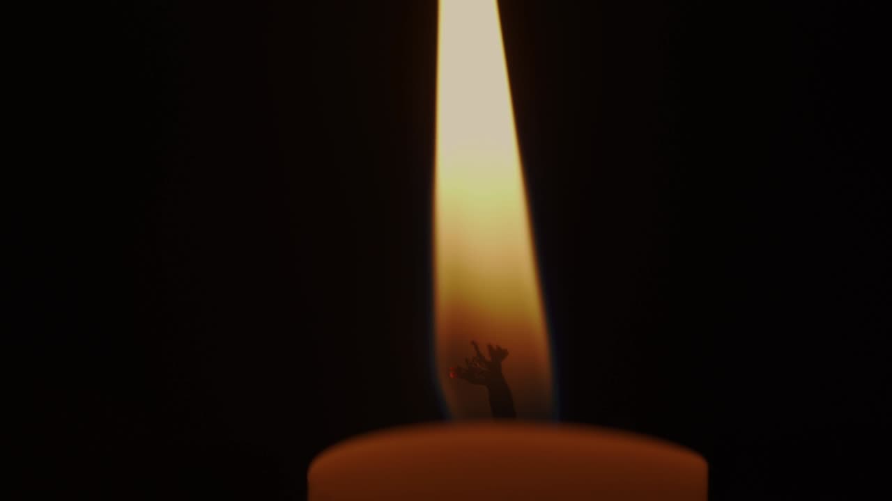 una llama de vela brillante ardiendo en el monumento en una habitación oscura.