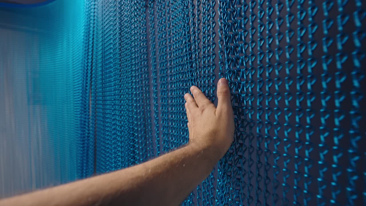 la mano pasa sobre los anillos metálicos azules del fondo de la cortina