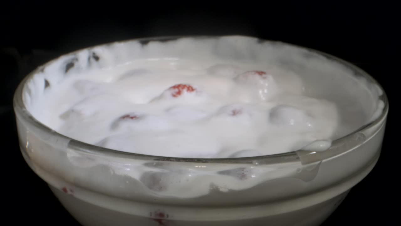 girar fresas maduras cubiertas con una capa gruesa de crema en vidrio sobre fondo negro. rotación de la cámara 360 grados, primer plano.