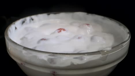girar fresas maduras cubiertas con una capa gruesa de crema en vidrio sobre fondo negro. rotación de la cámara 360 grados, primer plano.