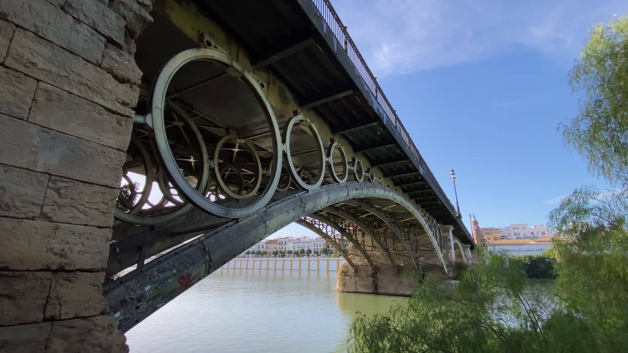 Triana Bridge seen through lush greenery and a bright lawn, a quiet riverside view in sunny Sevilla