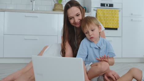 madre amorosa e hijos abrazados y divirtiéndose jugando sentados en el suelo. familia divertida y feliz. el juego después de ver la computadora portátil
