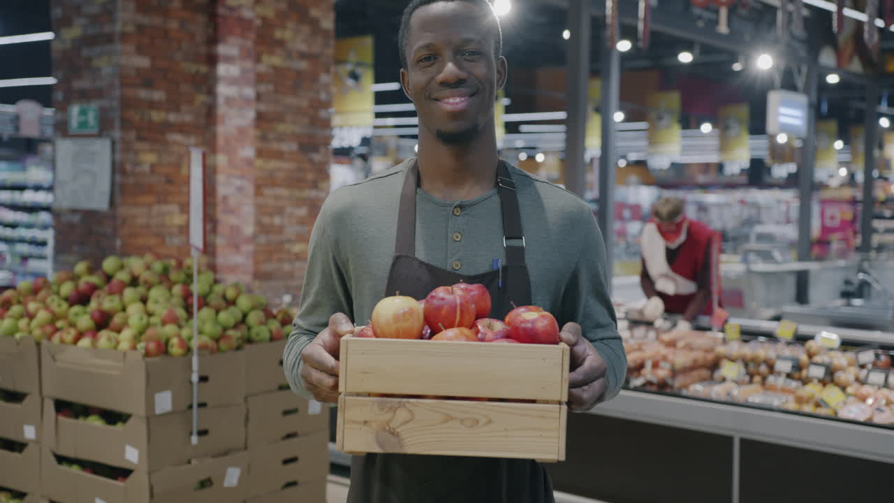 Dipendente sorridente di un negozio di alimentari che tiene una cassa di mele