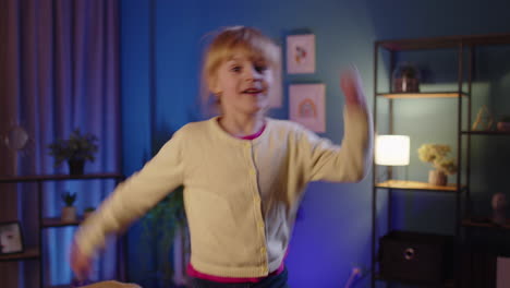 portrait happy toddler girl kid dancing trendy dance while listening to music at evening home alone