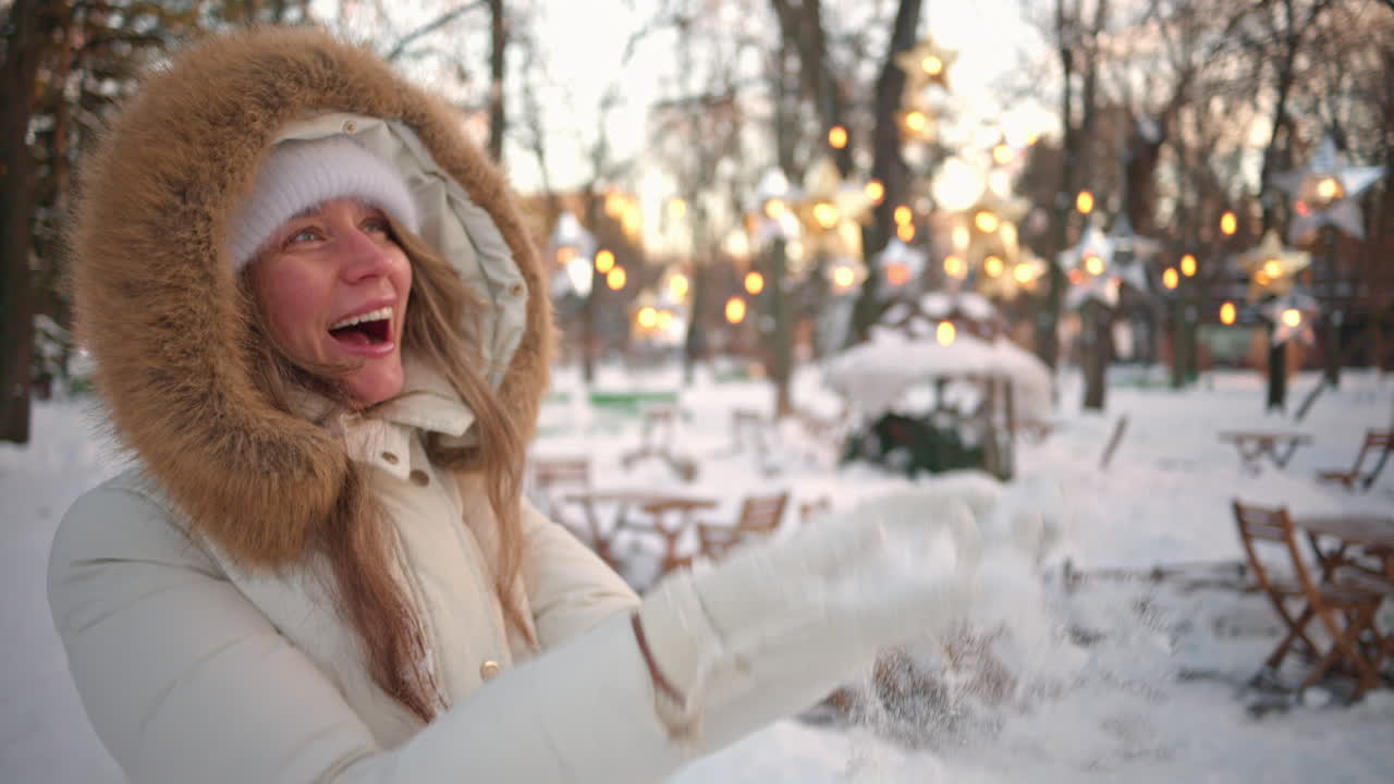 Woman having fun in winter throwing white snow in the air and smiling, slow motion
