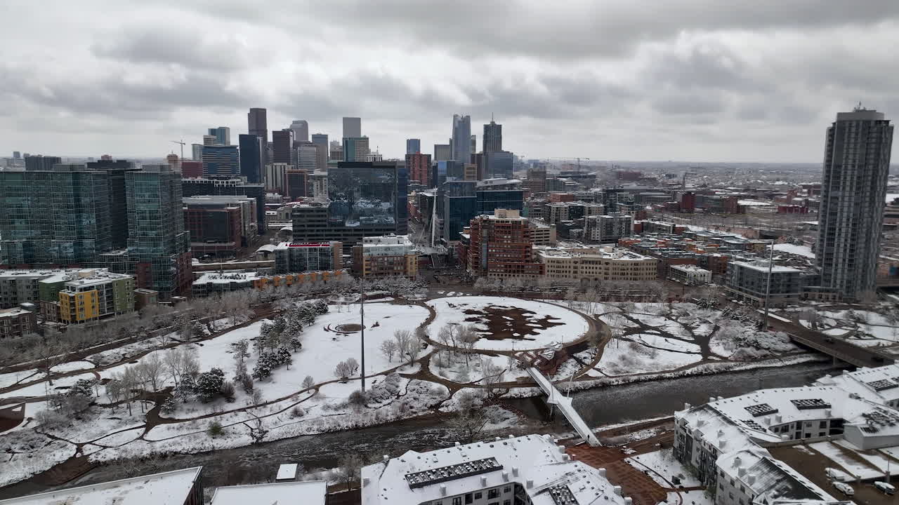 Ripresa aerea invernale del nevoso Commons Park con lo skyline di Denver contro un cielo grigio cupo.