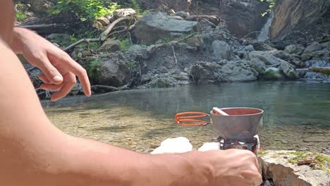 guy fires hobo cooker in nature and stir pot with soup on top