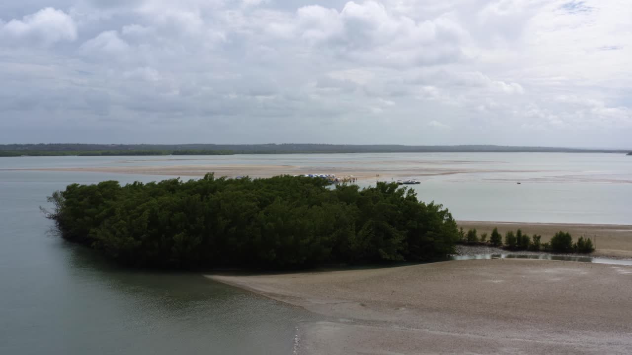 Dolly in aerial drone wide shot approaching a natural sand bar bank on the tropical Guara&iacute;ras Lagoon with tour boats umbrellas and food carts for tourists in Tibau do Sul Brazil in Rio Grande do Norte
