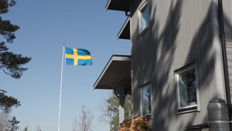 swedish flag on flag pole waving in heavy wind in slow motion next to villa