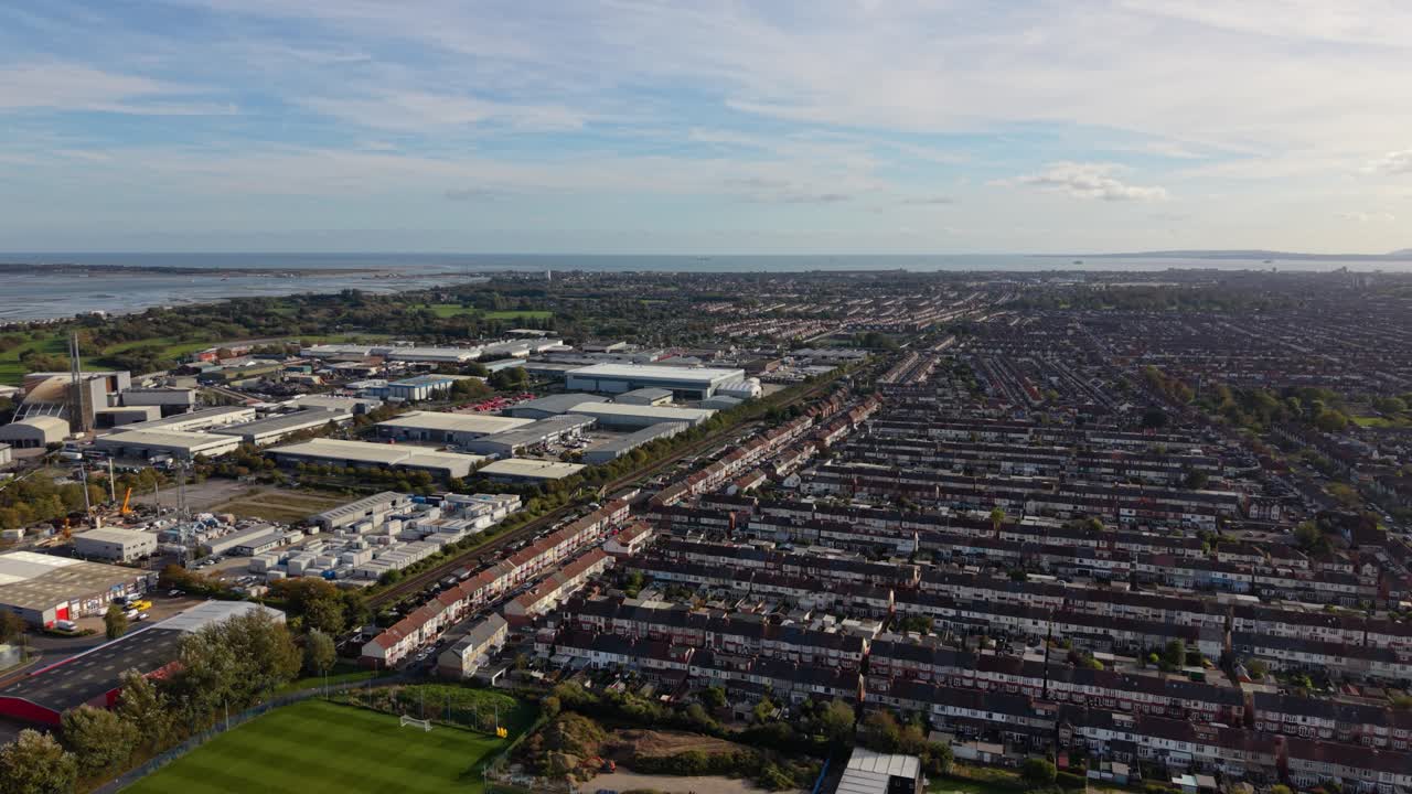 Volo di drone su Portsmouth, Regno Unito, sopra un'area commerciale vicino al porto, campo sportivo e spazi verdi, case a schiera con vista sul mare in una giornata di sole splendente, dettagliato e vario.