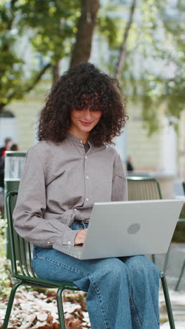 woman freelancer working online distant job with laptop browsing website sitting on city street