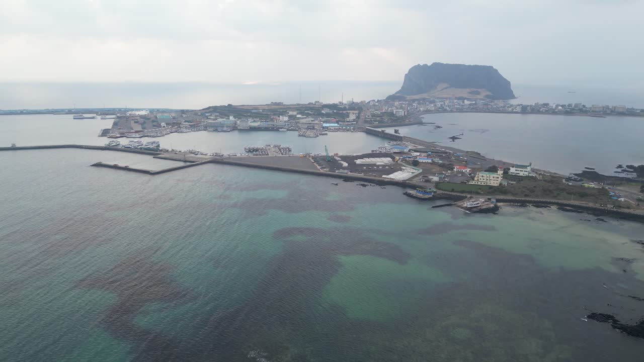 Drone aerial view in South Korea countryside flying over the ocean with a big green crater at sunrise small village island jeju island