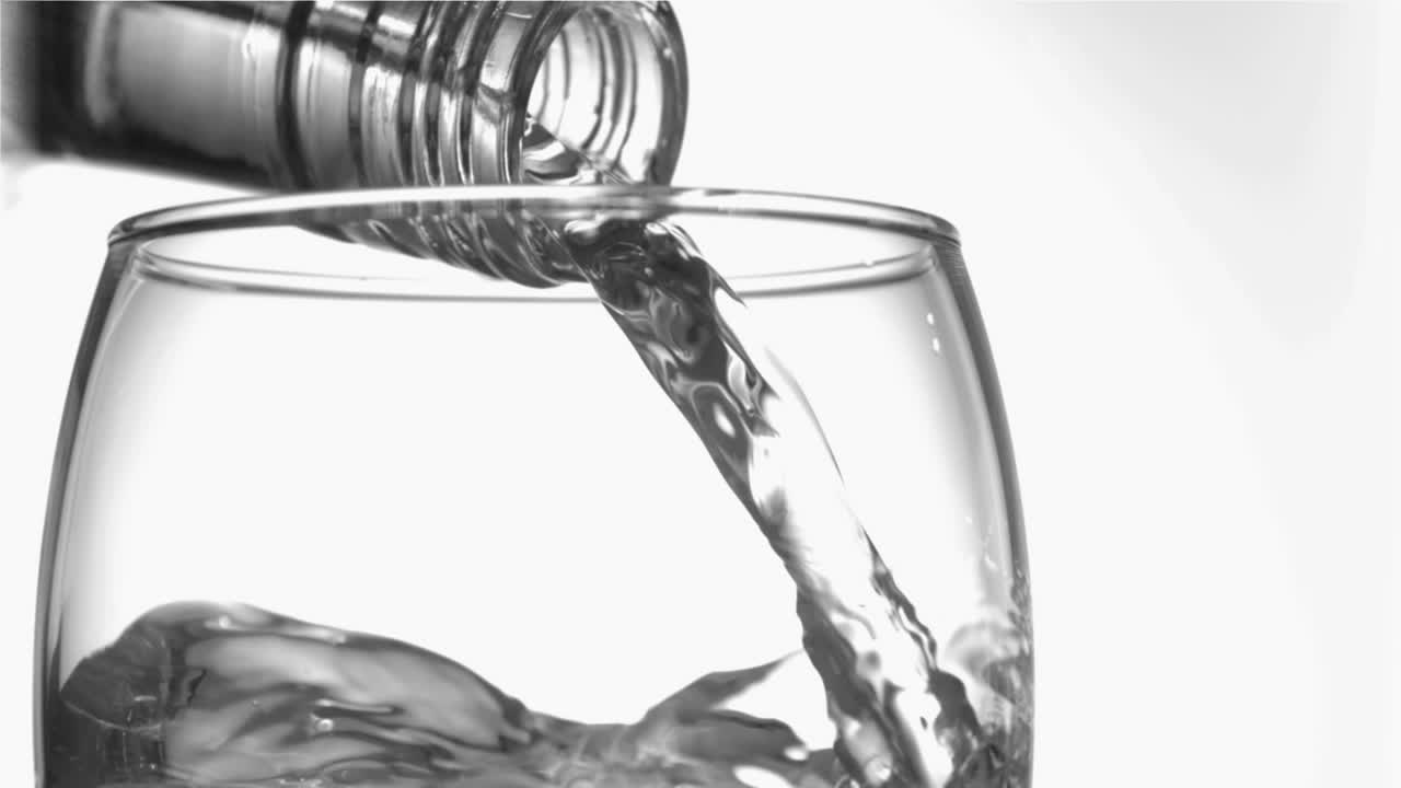 근처에서, 슈퍼 느린 움직임으로 물의 물이 유리 병목에서 유리병에 흐르고 있습니다.