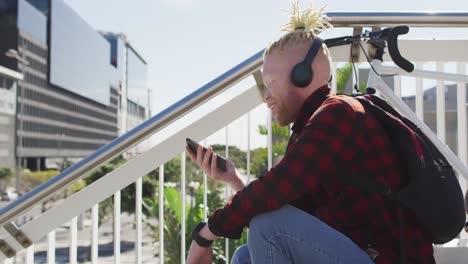 Happy-albino-african-american-man-with-dreadlocks-wearing-headphones-using-smartphone