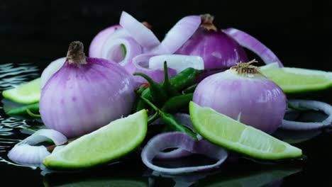 uncooked onion rings falling slow motion over organic green chilli and sliced lime isolated on black background