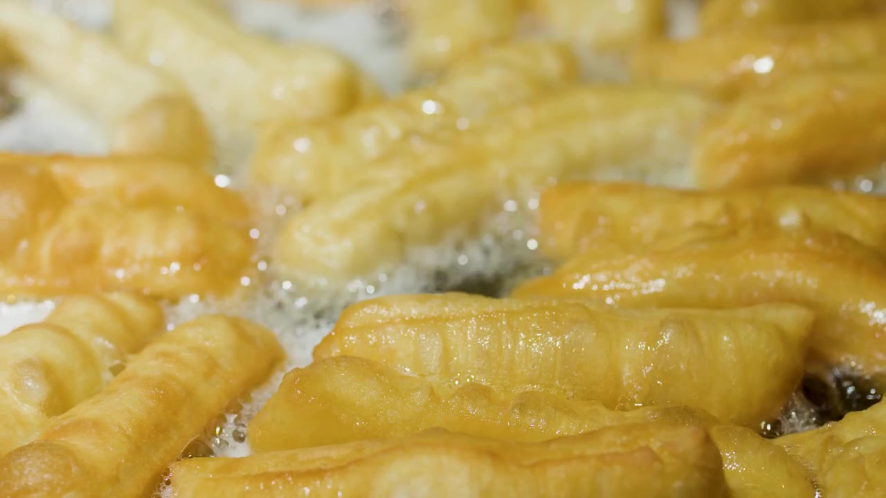 Primo piano di bastoncini di pasta youtiao dorati che friggono in una grande vasca di olio bollente