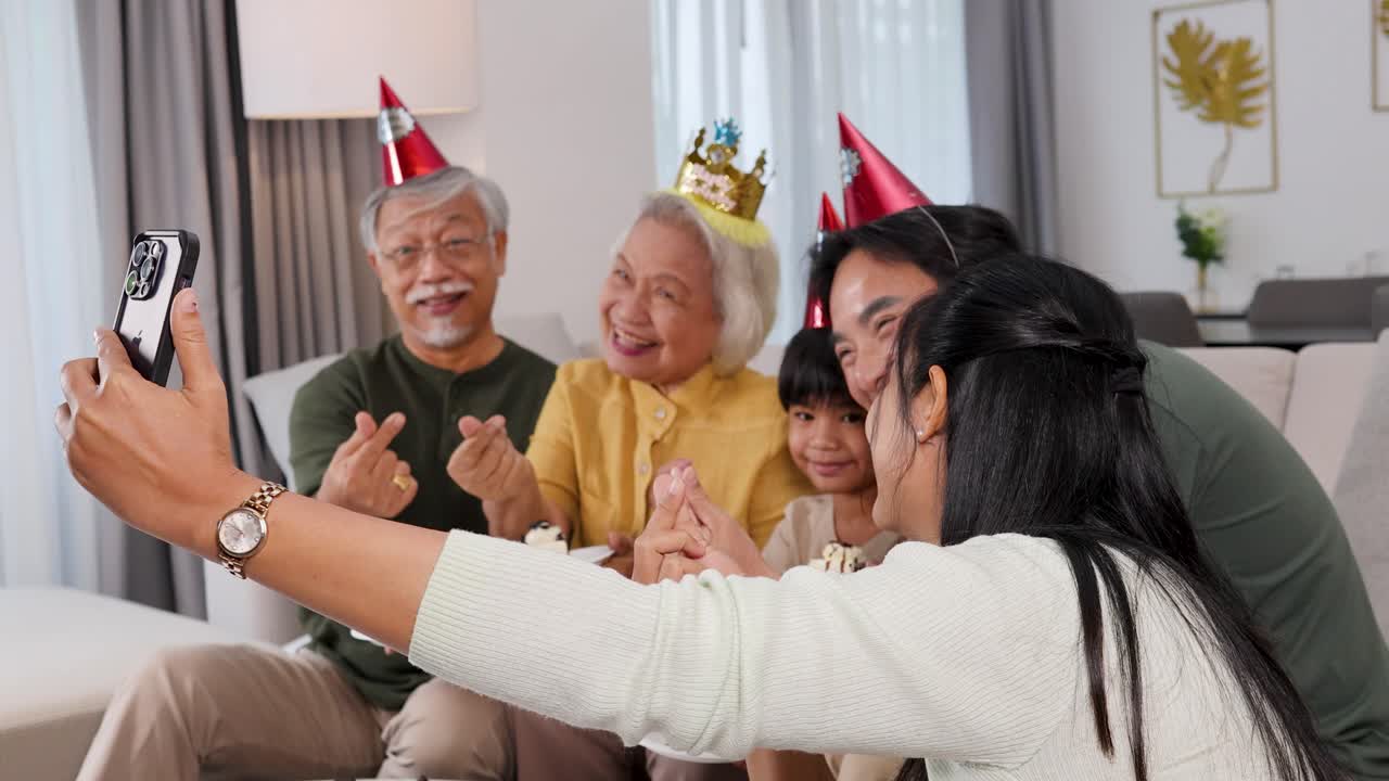 A joyful family captures selfies during a birthday celebration with cake. Warm lighting and festive hats create a cheerful atmosphere