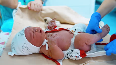 crying newborn id dressed by the gloved hands of medic. little child on the doctor's table. close up.
