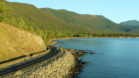 Scenic-Coastal-Drive-In-Queensland,-Cyclist-Riding-Bike-Around-Captain-Cook-Highway-Headland,-4K-Aerial-Drone