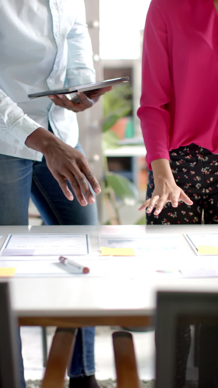 Vertical video of diverse colleagues discussing work with documents in office in slow motion