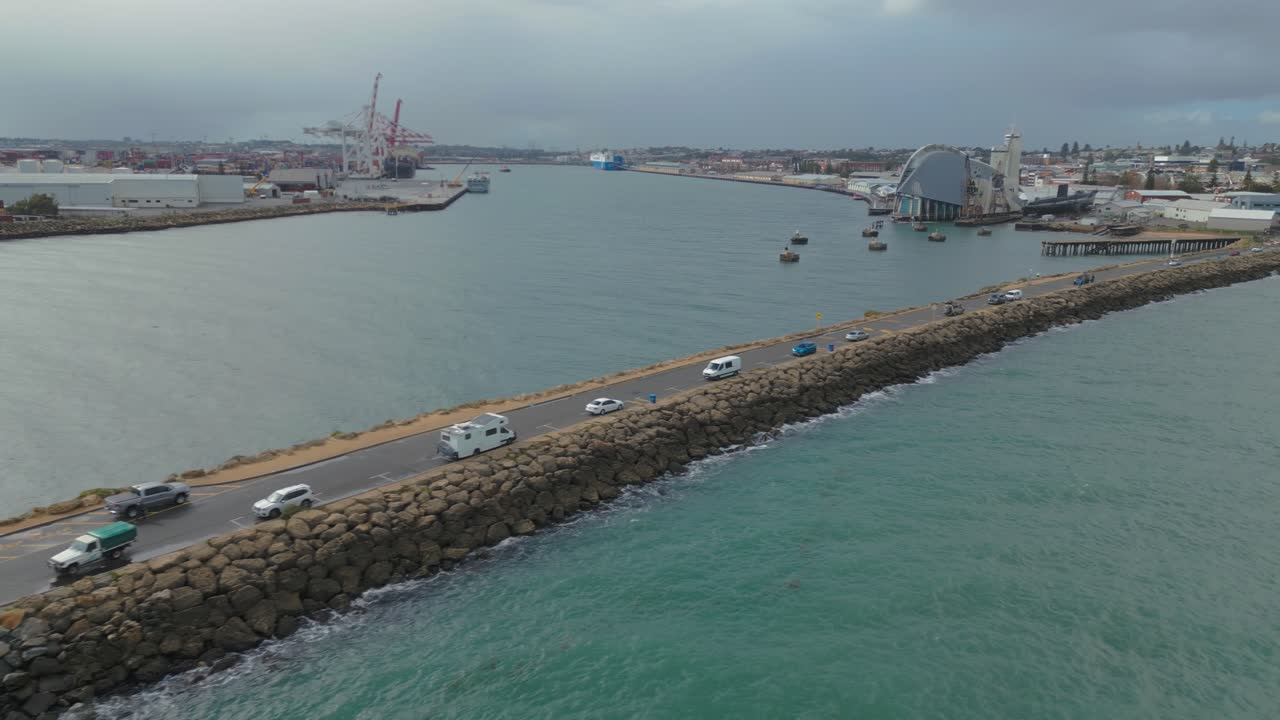 Drone footage pacing across the road from Fremantle towards the South Mole Lighthouse in Perth, Western Australia. Cars are parked along the road, where free parking is available