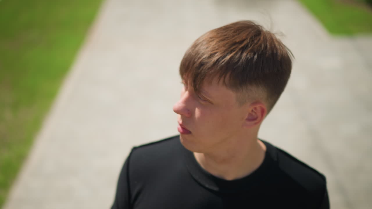 백인 남성이 야외에서 잠시 멈춰 서 있어요. 젊은 남성이 야외 활동이 계속되는 동안 주의 깊게 멈춰 서 있고, 젊은 백인 남성은 배경에서 야외 활동이 계속되는 동안 잠시 멈춥니다.