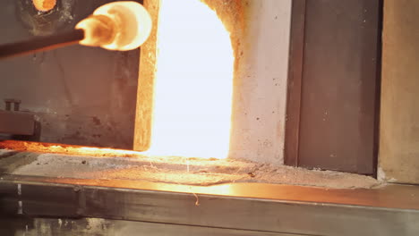 el artista del vidrio quita el vidrio fundido en la varilla del horno al rojo vivo en el estudio
