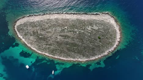 Rocky island surrounded by clear blue waters with boats near the shore in Kornati