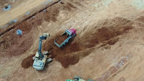 excavator loads dump truck at construction site - aerial perspective in 4k