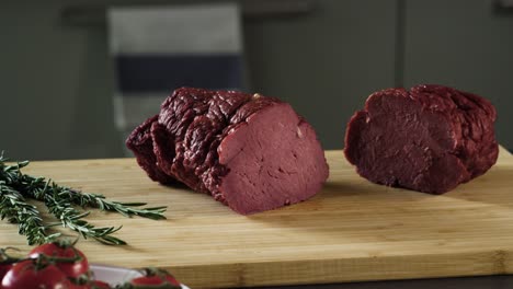 sliced cured beef on a wooden board with rosemary and tomatoes