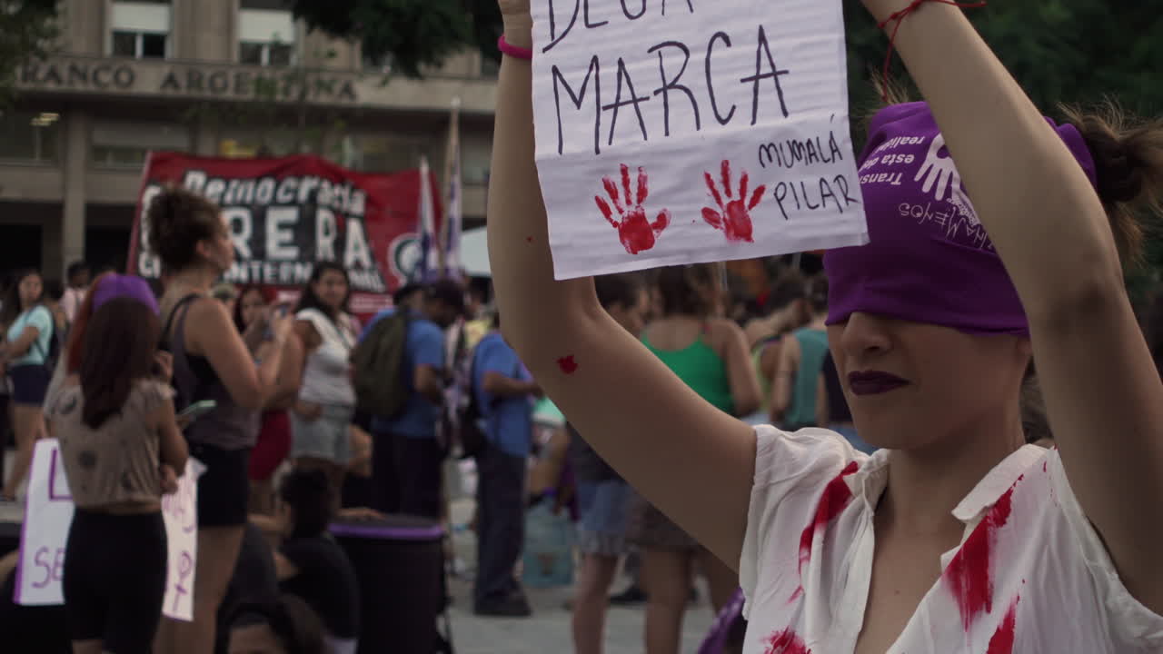 Close up of feminist activist with eyes covered with purple scarf on performance of gender violence and justice during abortion public event march