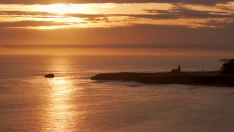 Slow-and-dramatic-pullback-drone-aerial-shot-of-sunset-over-ocean-with-surfers