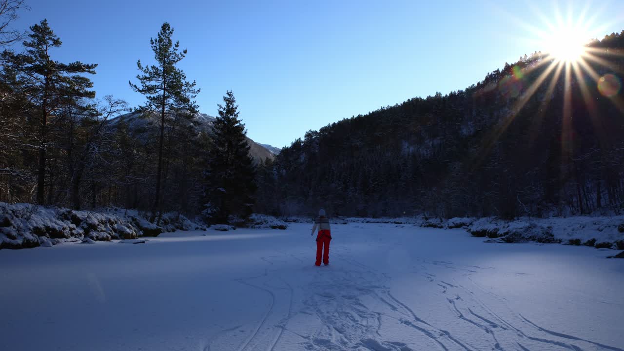 Young woman in sweater, bright red pants ice skating on frozen river during beautiful winter morning in Norway.