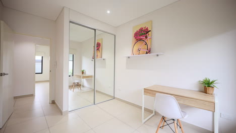 small bedroom with beige wooden and white accent desk and quirky painting by mirror sliding closet