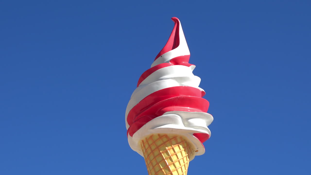 Low angle view of a large decorative red-and-white swirl ice cream cone sign against a clear blue