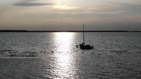 aerial view of silhouetted sailboat anchored on river with man walking along port side during early evening