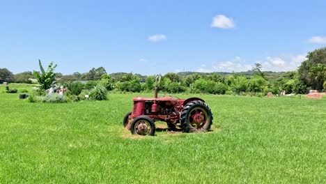 old red tractor progresses through a green pasture.