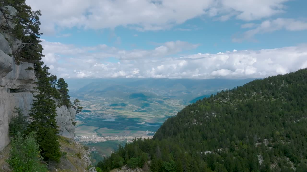 Hochalpine Bergansicht mit Blick auf ein Tal mit Wolken, Hügeln und Stadt.