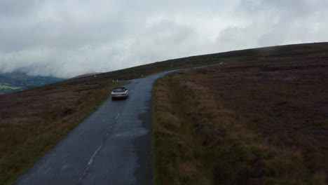 Two-cars-passing-by-each-other-on-narrow-wet-road-in-highlands.-Cloudy-autumn-day-at-large-moorlands.-Ireland