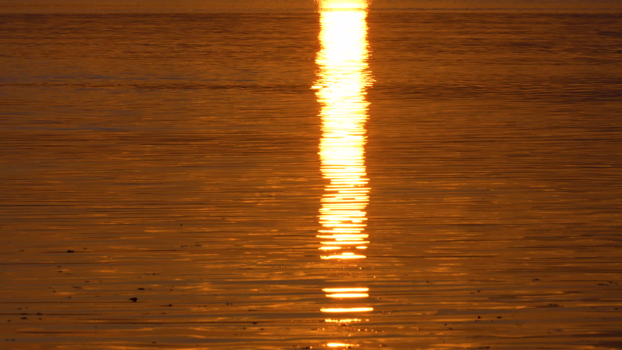 Bright sunrise reflection on calm ocean water creating a glowing vertical light path