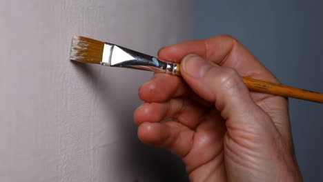 a close-up of a hand holding a paintbrush, applying paint to a canvas