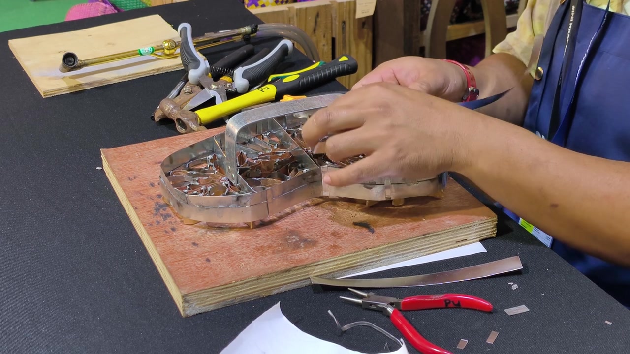 A craftsman creates a copper batik stamp. This traditional Malay art tool is dipped in hot wax to stamp patterns onto fabric. It saves time compared to hand-drawing.